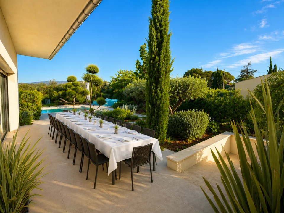 Grande tablée pour 16 personnes dressée sur la terrasse sud de la Villa Nirvana, jardin et piscine en arrière-plan
